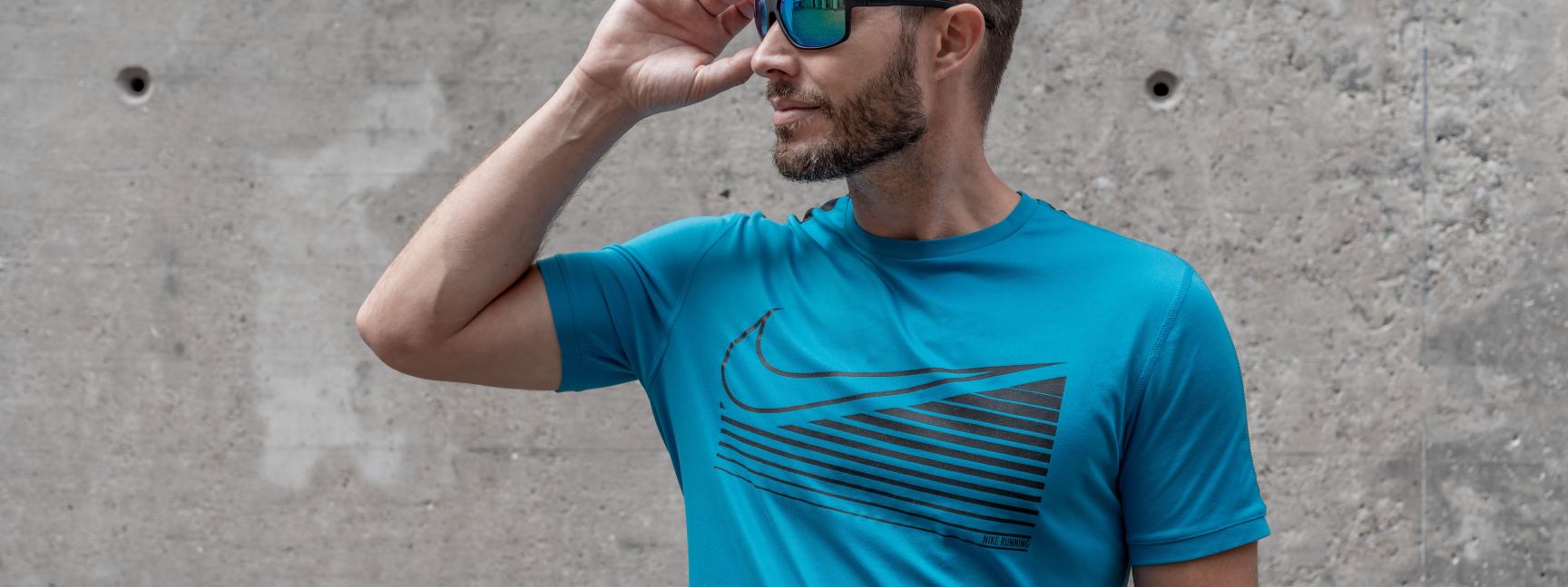 Ein Mann trägt zu seinem blauen T-Shirt eine blau verspiegelte Sportsonnenbrille.