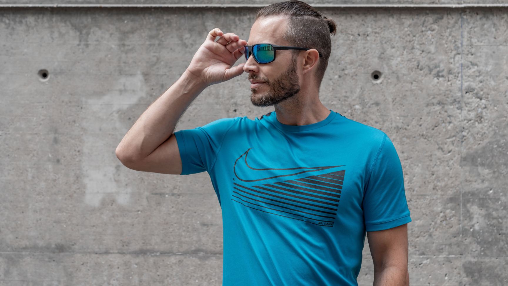 Ein Mann trägt zu seinem blauen T-Shirt eine blau verspiegelte Sportsonnenbrille.